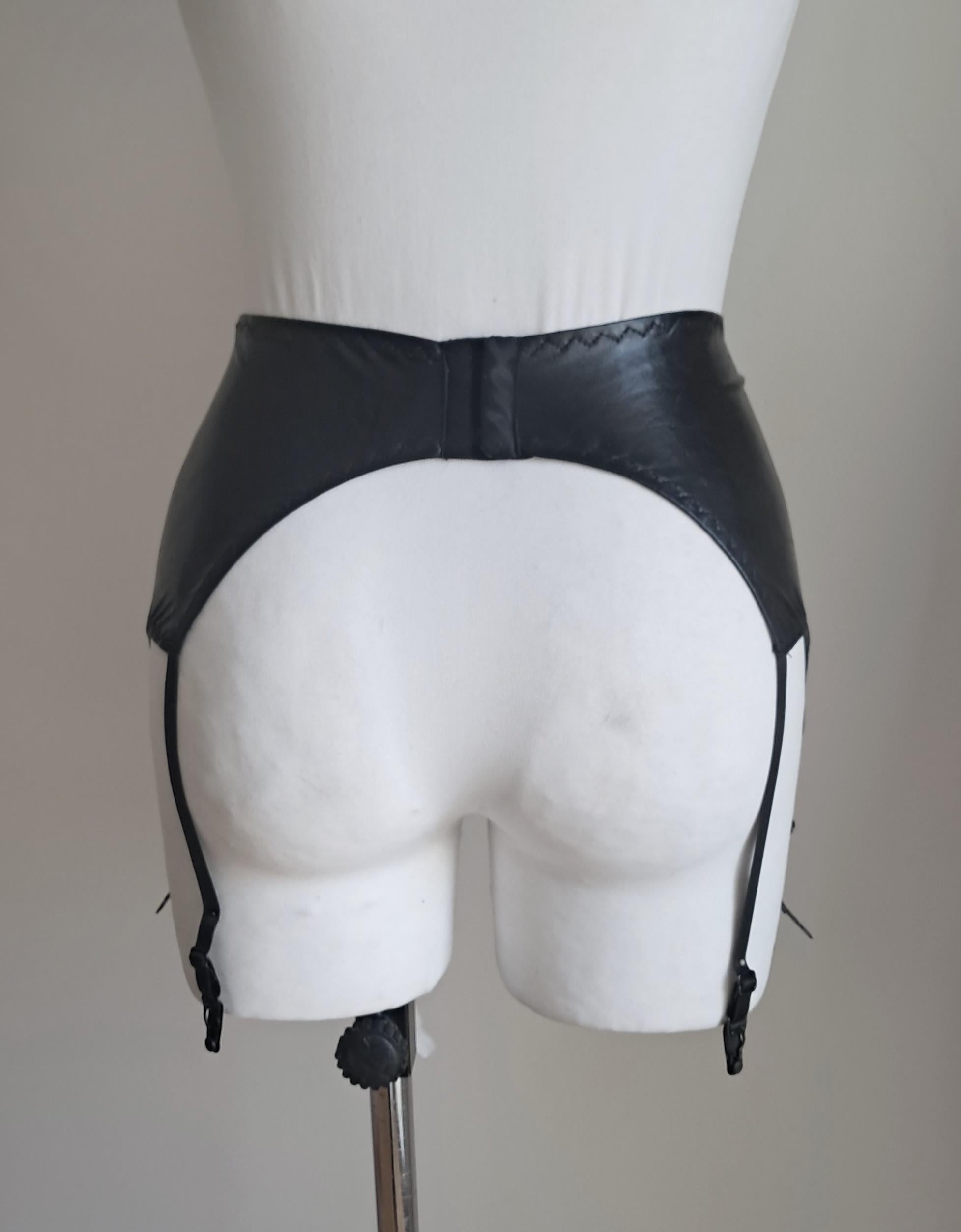 Black wet look garter belt on a mannequin against a plain background