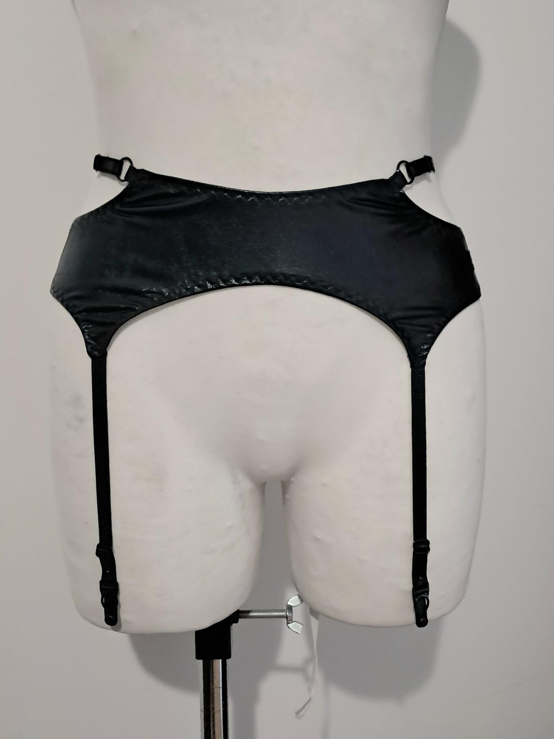 Black wet look strappy garter belt on a mannequin against a plain background