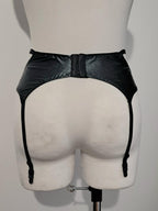 Black wet look strappy garter belt on a mannequin against a plain background